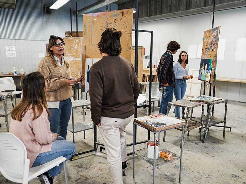 Mature teacher working with art students during painting class at school
