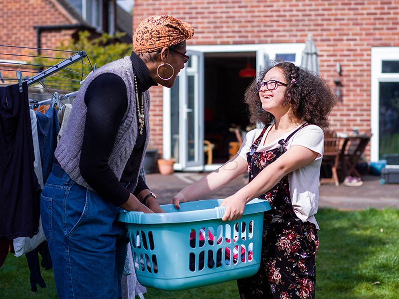 Mother with daughter carrying laundry basket across backyard