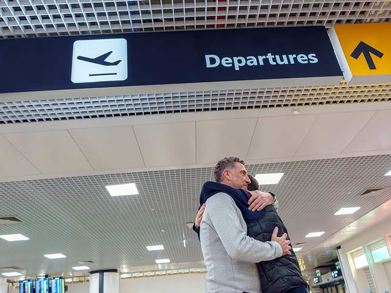 Father and teenage son embracing at the airport under the departures sign