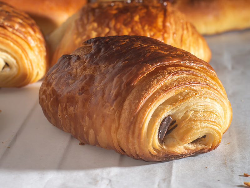Freshly backed french traditional croissant chocolate - petit pain au chocolat shiny in the rays of the morning sun.