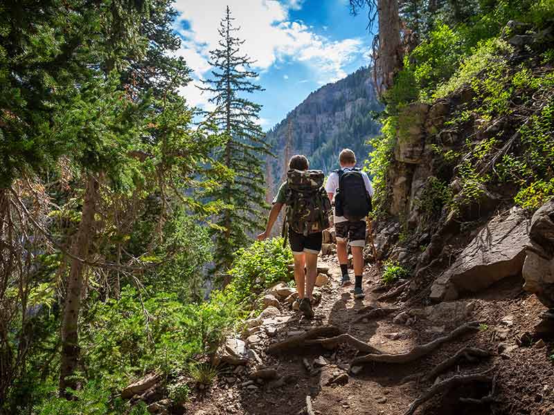 Two teen boys hiking together with backpacks up a rugged mountain trail
