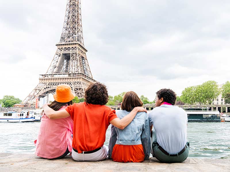 Multiethnic group of young happy teens friends bonding and having fun while visiting Eiffel Tower area in Paris, France