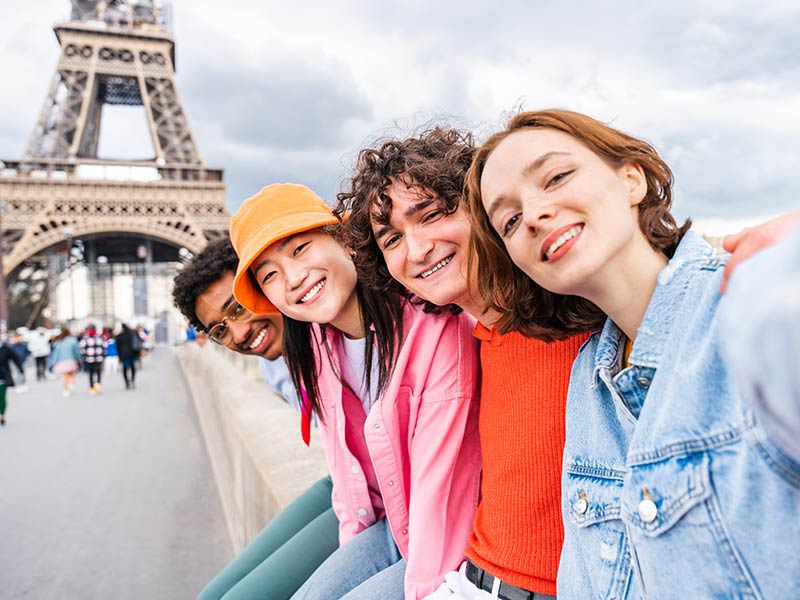 Multiethnic group of young happy teens friends bonding and having fun while visiting Eiffel Tower area in Paris, France