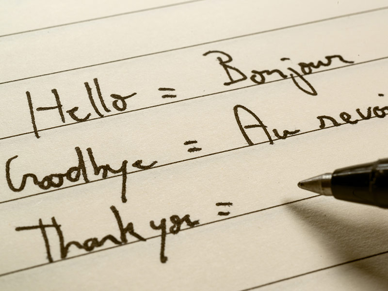 Beginner French language learner writing words in French for homework on a notebook